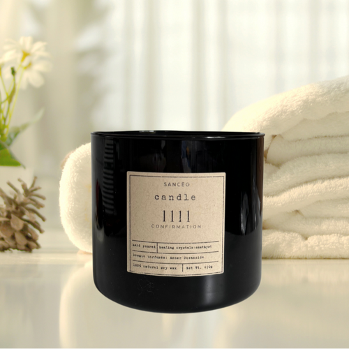 A black 20oz jar candle with a label that reads 'SANCEO 1111', placed on a white surface with a white towel and some foliage in the background.